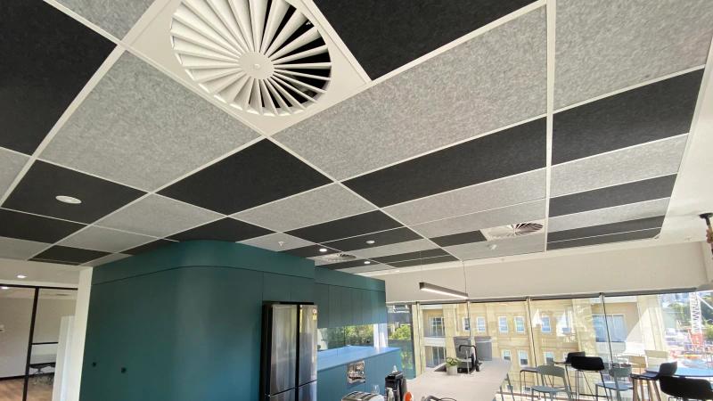 Acoustic ceiling tiles installed in an exposed suspended grid system, with air diffusers and downlights coordinated into the ceiling, in an Australian commercial office kitchen