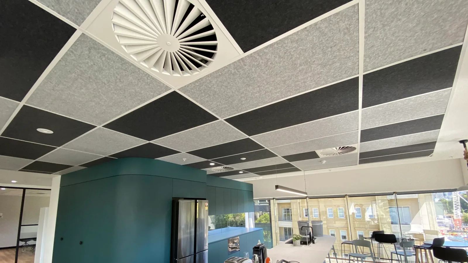 Acoustic ceiling tiles installed in an exposed suspended grid system, with air diffusers and downlights coordinated into the ceiling, in an Australian commercial office kitchen