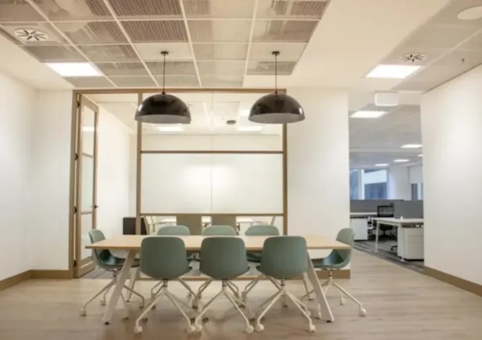 A meeting room with green chairs and a glazed partition, set under a continuous lay-in grid ceiling — Acoustic Panels Australia