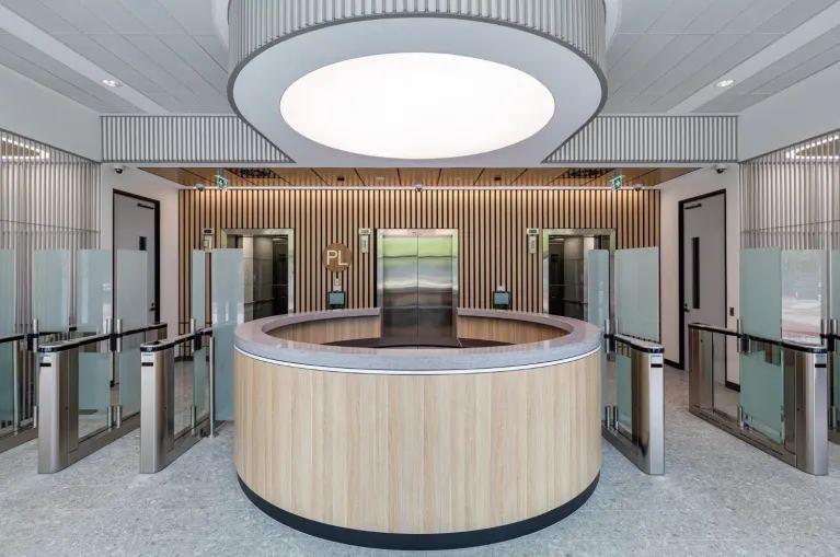 AUS Fins™ timber fin acoustic panels lining the walls of a reception lobby with a circular timber front desk and glazed entry — Acoustic Panels Australia