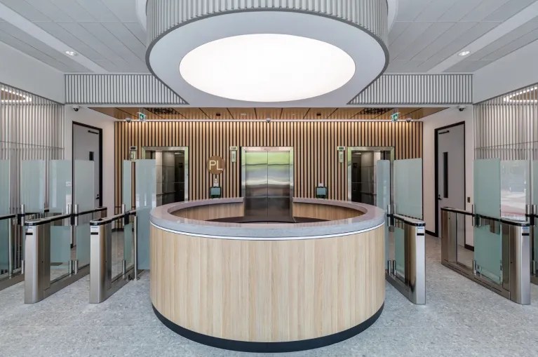 AUS Fins™ timber fin acoustic panels lining the walls of a reception lobby with a circular timber front desk and glazed entry — Acoustic Panels Australia