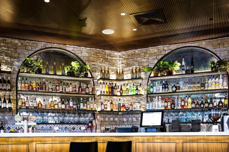 AUS Groove™ grooved timber acoustic panels across the ceiling of a bar, the linear profile adding warmth and depth above the stone feature wall and back-bar shelving — Acoustic Panels Australia